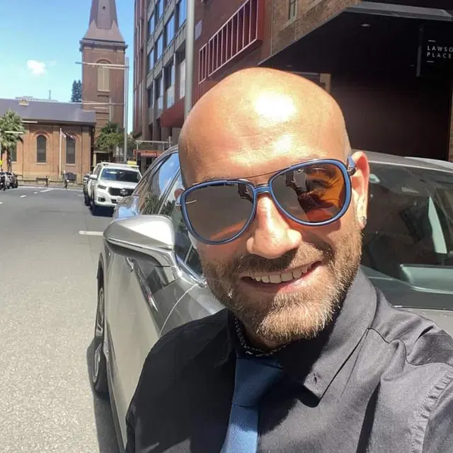 Jason Sildir, automotive writer and Car Sales Manager, in shirt and tie beside a silver sedan on a Sydney street